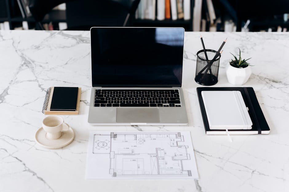 Modern minimalist workspace featuring a laptop, notebook, and blueprints on a marble table.