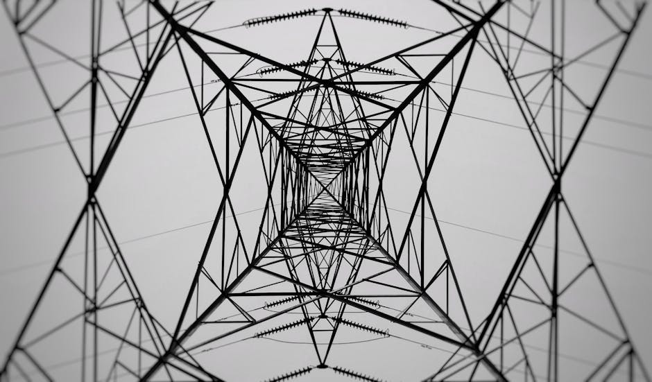 Monochrome low-angle shot of a power transmission tower in symmetrical perspective.