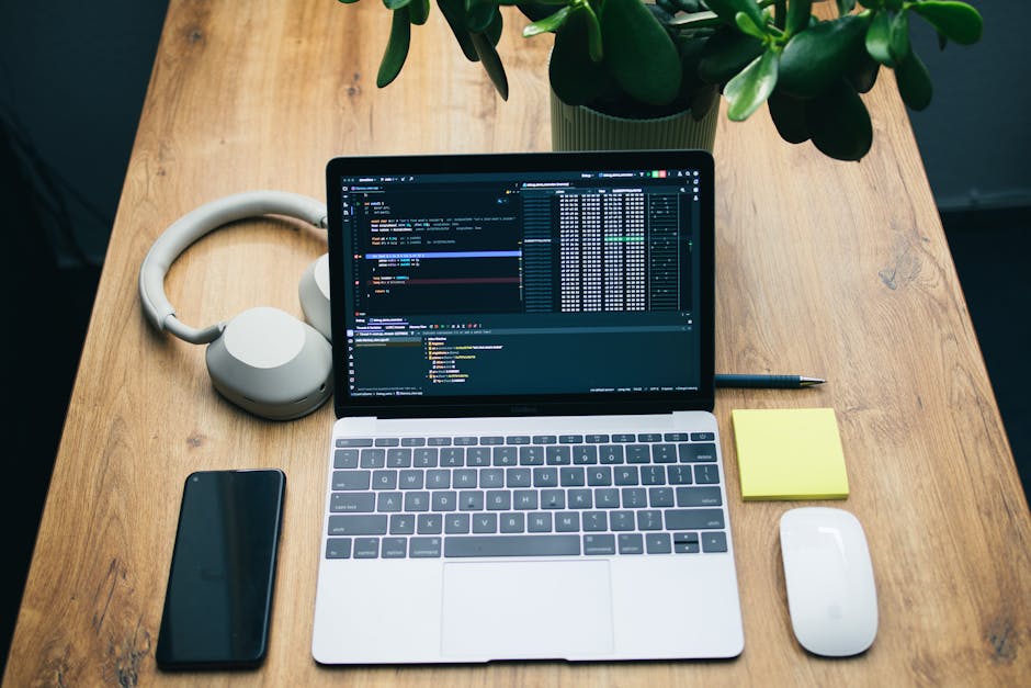 A clean and modern workspace featuring a laptop, headphones, smartphone, and a houseplant.