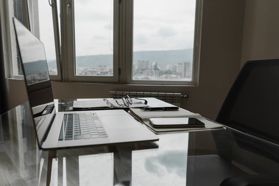 A sleek office setting with a laptop, notebook, and city skyline view through the window.
